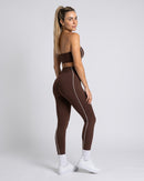 Conjunto café de costas, com a linha branca na lateral da legging (imagem criada com IA)