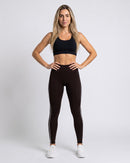 Mulher com a Legging Cintura Alta marrom escura com friso branco, de frente (imagem criada com IA)