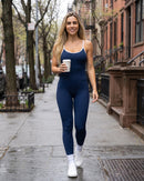 Modelo com o macacão azul-marinho caminhando na rua com um café (imagem criada com IA)